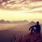 Tall hiker in dark shirt sit on a rockatn heather bushes, enjoy misty morning scenery