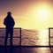 Tall man stand on mole wooden board and looking over ocean to Sun. Empty wharf,