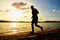 Tall man with sunglasses and dark cap is running on beach at autumn sunset