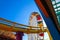 A tall metal Ferris wheel with colorful cars around the wheel on with a yellow rollercoaster rail and blue sky