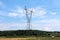 Tall metal power line connected with multiple wires high above cornfield and forest