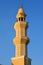 A tall minaret with golden ornament of a mosque against blue sky, minaret or tower aspiring to heaven