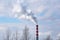 A tall, multi-colored concrete chimney emits puffs of smoke into the atmosphere