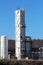 Tall old white rectangle storage silo rising above row of brand new storage silos at oil refinery complex