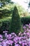 A tall ornately trimmed green bush with flower beds with small p