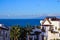 A tall palm tree and white houses with brown roofs against the ocean and blue sky. Gia de Isora, Tenerife