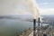 Tall pipes of power plant, white smoke on rural landscape, lake water and blue sky copy space background