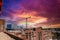 Tall red brick buildings and glass skyscrapers with tall tower cranes in the cityscape with red sky and powerful clouds at sunset