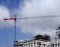 Tall red crane on a large construction site with metal framework scaffolding blue sky and clouds