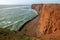 Tall red dramatic cliffs of Heligoland island with rough sea. Sunny windy winter day in Helgoland in the North sea