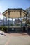 A tall round green pergola in the middle of a courtyard surrounded by people, lush green trees and buildings