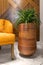 Tall rounded wooden planter with green bushes, beside orange armchair, wood cladding decorated wall, and marble floor