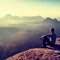 Tall short hair hiker in light shirt sit on a rock and enjoy foggy mountain scenery