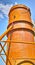A tall silo water tower against a blue sky background from below. An orange storage tank for the farming or agriculture