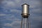 Tall silver water tower in front of a cloudy blue