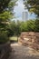 Tall skyscraper in distance of curving rock walled sidewalk through wooded urban park