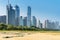Tall skyscrapers of a modern, metropolitan cityscape tower over a beautiful, white, sandy beach