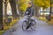 Tall smiling guy of European appearance in glasses, with a yellow scarf and a gray jacket rides a Bicycle along the Avenue of the