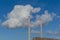 Tall smokestack chimneys of an industrial port factory under a blue sky and white clouds