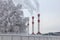 Tall, smoking pipes of a thermal power plant and frozen trees in winter