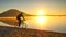 Tall sportsman pushing bicycle in sand of mountain lake beach, colorful sunset cloudy sky in background and reflection in water