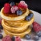 Tall stack of pancakes with raspberries, blueberrie and powdered sugar