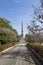 A tall stone confederate monument in the center of the confederate burial grounds with lush green trees, plants and grass