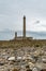 Tall stone lighthouse with rocky shore at low tide under a stormy sky