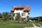 Tall suburban family house with dilapidated white yellow facade and faded color on roof tiles surrounded with uncut grass and