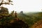 Tall tourist climbing on sharp cliff and overlooking beautiful view above forest valley bellow.