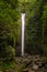 Tall waterfall in jungle forest, falling into the mountain river with stone riverbed.