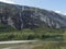 Tall waterfall with turquoise Rauma river at Romsdalen valley with rocks and green forest. Blue sky white clouds background.