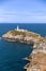 Tall white stone lighthouse at the edge of a rocky island cliff on a rugged coastline. South Stack Lighthouse