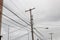 Tall wood power pole with insulators, transformer, street lamp and assorted lines against a gray sky