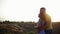 Tall young bearded guy in polo shirt hugs behind pretty girl in striped dress and hold hands in field against defocused