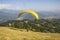 A tandem paragliders on a yellow parachute during takeoff from the hillside against the background of green mountains and the city