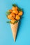 Tangerine fruits in waffle ice cream cone on blue background. winter Christmas food concept. vertical orientation