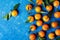 Tangerines or mandarins with green leaves on vintage blue table top view in flat lay style.