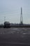 Tank in a parking lot by the edge of a fields with a pylon on a cloudy day