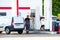 A tanker refueling a white van at a gas station.