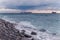 The tanker ship sails on the sea horizon. Stone coast and sea waves in the foreground