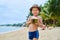 Tanned Asian boy stands on the beach in a hat and drinks coconut