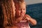 Tanned baby girl in pink swimsuit sucks her finger in the summer at sea