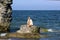 Tanned blonde in white dress and sunglasses sits on a stone on the shore of the Baltic Sea. Sunny day