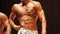 Tanned bodybuilder posing on stage at athletic competition, perfect male body