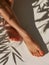 Tanned female legs with smooth skin and red nail polish on toes. Elegant feet on white sand with shadows. Generative AI