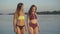 Tanned happy young women in swimsuits walking along river bank at sunset and talking. Portrait of joyful beautiful