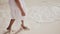 The and tanned legs of an philippine schoolgirl in a white dress walk on white sand, touching the foamy waves by