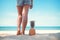 Tanned legs of young woman standing with pineapple at tropical beach in summer