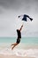 Tanned man jump with umbrella in blue sea